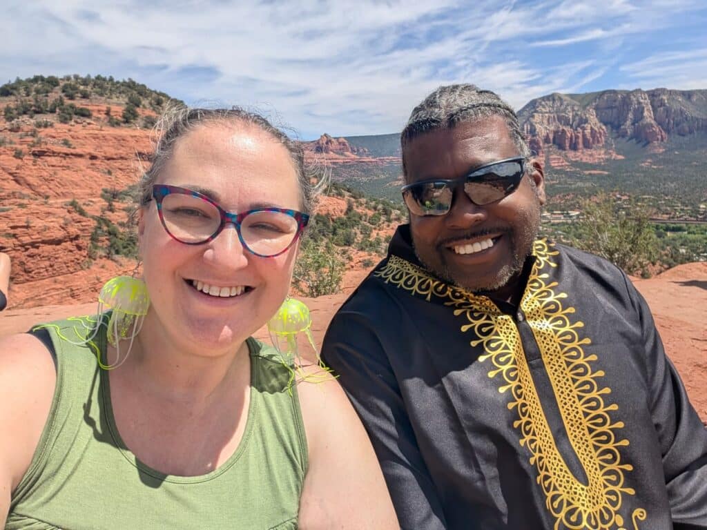 Sadie Smiley on the left, wearing jellyfish earrings and a green shirt. Kevin on the right, wearing his sunglasses, braids, and a black and gold African robe. They are atop the Airport Mesa Vortex.