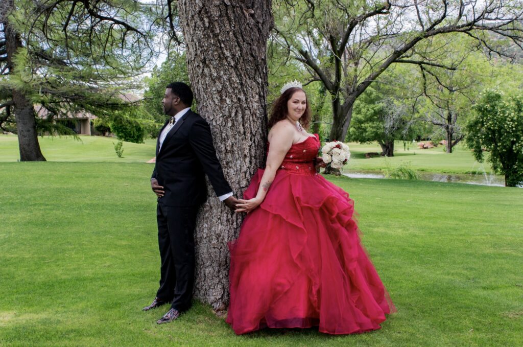 Kevin Smiley standing on the left of a tree, in Sedona, at his wedding with Sadie Smiley, standing on the right in a red dress